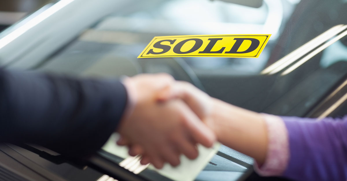 Buyer and seller shaking hands with sold sticker on car in background